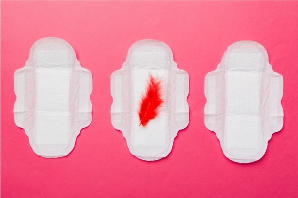 Trije vložki, na srednjem rdeče pero, ki ponazarja menstruacijo.