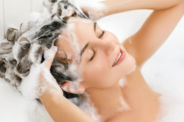 mlada ženska si pere lase z nežnim šamponom. Seboroični dermatitis lasišča.